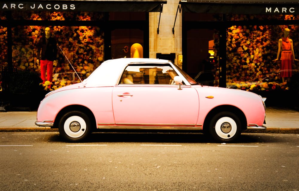 Pink vintage car parked on street with store sign